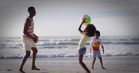 Tossing large pastel-colored beach ball between father and two children at water's edge. Family, outdoor, leisure, playful, vibrant, activity, bondingの写真素材