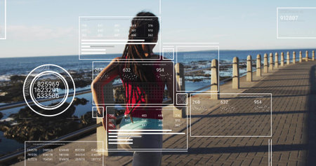 Standing woman wearing red top, gray leggings scanning ocean on walkway, with shoreline, AR panels. Futuristic, coastal, outdoor, technology, fitness, relaxation, sceneryの写真素材
