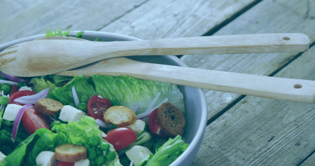 Showing grey salad bowl holding salad mix with cheese cubes, croutons and wooden servers on table. Healthy, freshness, organic, rustic, vibrant, natural, cuisineの写真素材