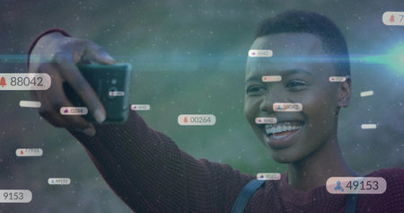 Smiling creator in sweater taking selfie with smartphone in park with floating notification icons. Lifestyle, social media, outdoor, technology, influence, communication, vibrantの写真素材