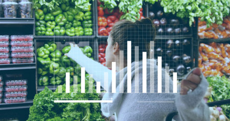 Reaching woman wearing knit sweater in bun selecting green peppers in produce aisle, with bar chart. Fresh produce, grocery shopping, healthy eating, organic, consumer behavior, retail, colorfulの写真素材
