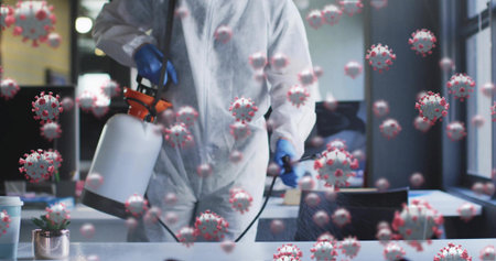 Spraying technician in coverall using sprayer on office desk with coronavirus particles, copy space. Disinfection, sanitation, germ protection, hygiene, health, cleanliness, workplace safetyの写真素材