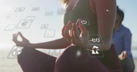 Practicing woman wearing activewear meditating on sandy shore at sunrise, with floating eco icons. Wellness, mindfulness, serenity, eco-friendly, sustainability, nature, tranquilityの写真素材