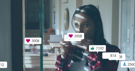 Woman standing by blinds in kitchen, with coffee cup, books, straw hat, copy space. Sunlight, interior, lifestyle, cozy, communication, leisure, modernの写真素材