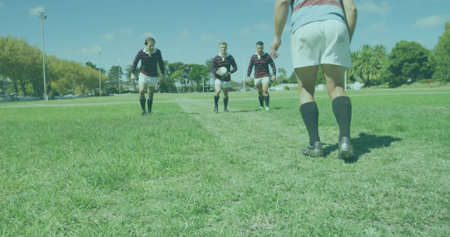 Walking rugby teammates approaching player from midfield line on grass field, with rugby ball. Athletics, teamwork, outdoor, leisure, energy, sportswear, competitionの写真素材