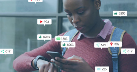 Woman in sweater and backpack holding smartphone and checking smartwatch at window, icons floating. Urban, fashion, casual, technology, modern, lifestyle, empowermentの写真素材