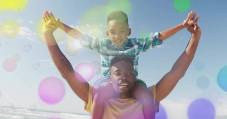 Carrying man hoisting boy balancing arms outstretched on sandy shore, with colored light flares....