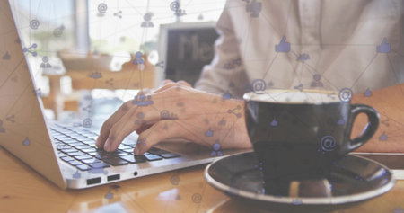 Typing writer tapping silver laptop at cafe beside black coffee cup, floating social icons. Concentration, productivity, digital, communication, workspace, modern, relaxedの写真素材