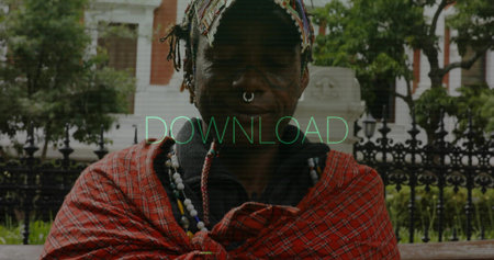 Standing man wearing head wrap, red shawl on bench in park, with iron fence, septum ring. Heritage,...