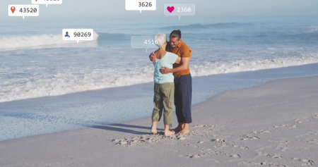 Embracing senior couple standing on sandy beach at water edge, with floating digital overlays....