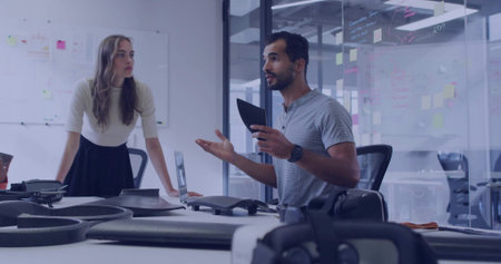 Presenting engineer holding tablet gesturing at drone prototypes in office with whiteboard sketches....