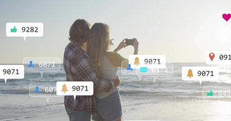 Taking smartphone selfie couple in casual attire hugging at sunset shore, with social media icons. Romance, outdoors, leisure, digital, serene, connection, modernの写真素材
