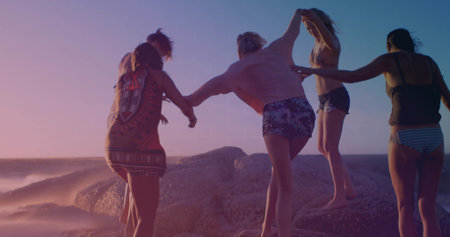 Balancing five women in swimwear walking hand-in-hand on coastal rocks at sunset with sunglasses. Adventure, friendship, harmony, leisure, nature, travel, warmthの写真素材