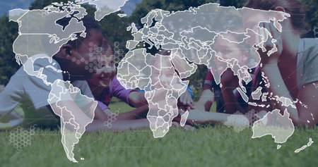 Lying diverse children studying tablet computer on lush green lawn in park, with world map overlay....