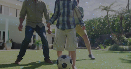 Playing three-generation family kicking soccer ball in suburban backyard, with fence, palm tree....
