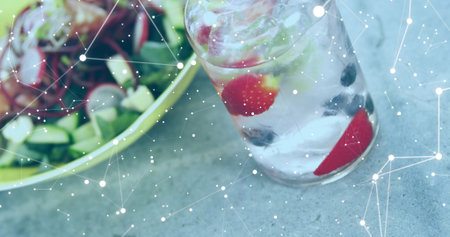 Showing glass holding iced fruit-infused water mint beside salad bowl on stone tabletop, copy space....