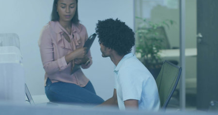 Holding black tablet, woman wearing pink blouse, speaking to coworker in office with silver laptop. Professional, collaboration, communication, modern, workspace, teamwork, businessの写真素材