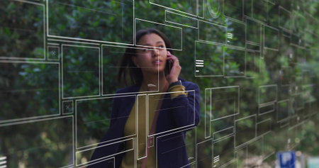 Walking business woman in navy blazer talking on smartphone on pedestrian path, with AR panels. Technology, innovation, connectivity, outdoor, professional, vibrant, modernの写真素材