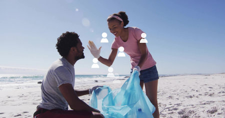 Collecting litter gloved shore cleanup volunteers working on sandy beach, holding blue bag. Environment, conservation, teamwork, eco-friendly, sustainability, outdoor, natureの写真素材
