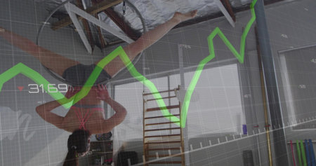Holding inverted split athlete in sportswear gripping metal ring in studio, with line graph overlay....
