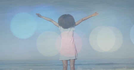 Woman in white sundress standing barefoot at shoreline, with ocean waves horizon lens flare circles. Seascape, serenity, minimalism, relaxation, freedom, natural light, coastalの写真素材