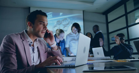 Man in blazer talking on smartphone while typing on laptop in meeting room, with projection screen. Collaboration, innovation, technology, modern, professional, teamwork, digitalの写真素材