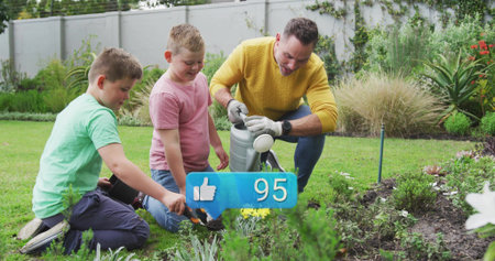 Tending man in yellow sweater and boys kneeling on backyard lawn, with watering can, trowel, gloves....