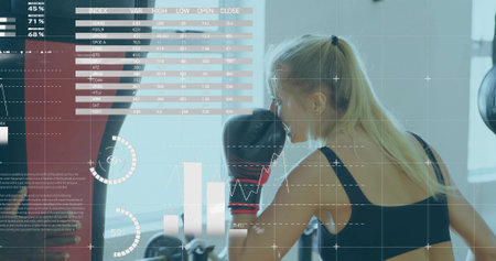 Throwing punch trainee wearing boxing gloves striking heavy bag in gym, displaying data overlays. Athletic, fitness, training, technology, health, strength, performanceの写真素材