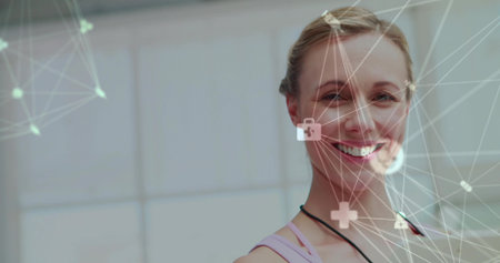 Smiling woman in sports top showing overlay in studio with padlock, medical icons, frosted panels. Futuristic, technology, innovation, cybersecurity, health, connectivity, digitalの写真素材