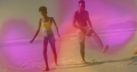 Couple in yellow top and swim trunks walking at sunny beach shore, kicking water splashes. Seascape,...