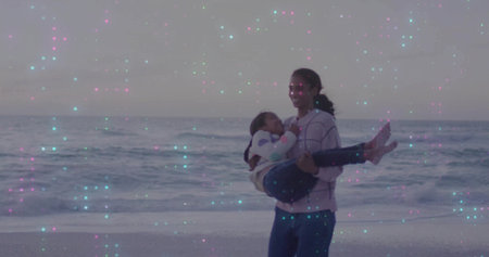 Mid adult woman holding school-age child at ocean beach water's edge at dusk, with light artifacts....