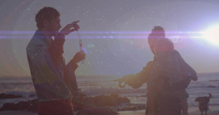Holding bubble wand, couple blowing bubbles on rocky shore at sunset, with lens flares and dog....