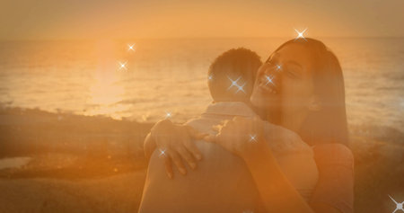 Hugging couple wearing casual clothes on rocky shoreline at sunset, with golden sparkle effect. Romance, nature, serenity, affectionate, outdoor, tranquility, warm tonesの写真素材