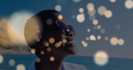 Smiling woman wearing aviators and striped shirt at rocky shoreline, with bokeh overlay, copy space. Casual, outdoor, vibrant, optimistic, lifestyle, scenic, fashionの写真素材