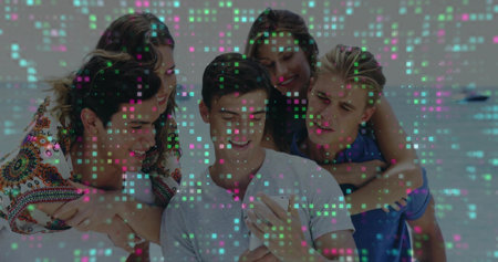 Huddling group of five friends in summer clothing on sandy beach by sea, viewing smartphone. Beach, friendship, leisure, outdoor, casual, lifestyle, happinessの写真素材