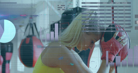 Pausing female athlete leaning on red punching bag in gym, wearing red gloves with chart overlays. Fitness, training, performance, wellness, sport, health, strengthの写真素材