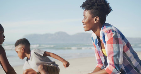 Watching woman in plaid shirt crouching at shore interacting with children on beach, copy space....