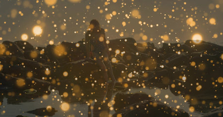 Standing woman wearing jacket at coastal tidal pools, with dark rocks and glowing light particles. Nature, landscape, serenity, adventure, tranquility, reflection, duskの写真素材