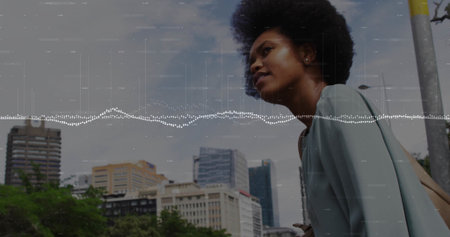 Standing African American woman in blue coat, carrying beige bag on downtown walkway, copy space. Urban, skyline, modern, professional, casual, architecture, cityscapeの写真素材