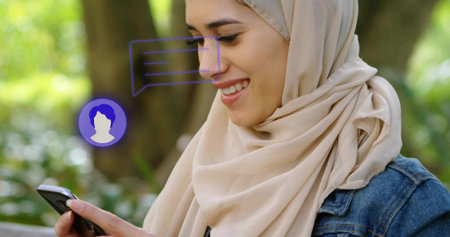 Texting hijab-wearing woman at park bench with smartphone chat bubble and avatar icons, copy space....