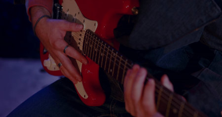 Showcasing musician hands strumming red electric guitar in studio, with metal rings and bracelet....