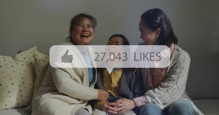 Laughing family sitting on sofa at home with polka-dot pillows. Family, togetherness, warmth, casual, cozy, harmony, generationalの写真素材