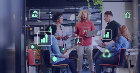 Gathering five professionals reviewing data overlays in open-plan office, with laptop, tablet, and...