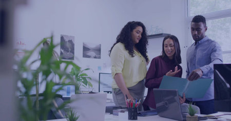 Three professionals reviewing document at modern office white desk, with laptop and blue folder....
