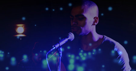 Singing vocalist focusing on microphone on dim stage, with warm spotlight and drifting light orbs. Performance, music, ambiance, lighting, artistry, concert, entertainmentの写真素材