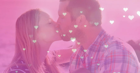 Leaning mid adult couple kissing against soft pink-hued backdrop, with heart-shaped overlays. Romance, affection, intimacy, couple, passion, dreamy, tendernessの写真素材