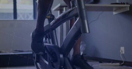 Pedaling male wearing black athletic shorts, sneakers on exercise bike at gym, with desk cables....