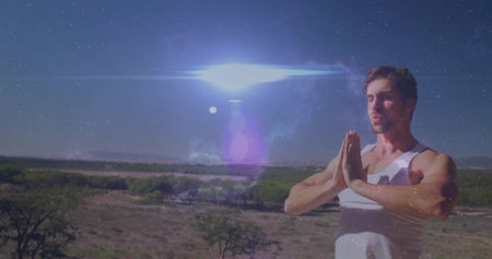 Meditating man wearing white tank top pressing hands together on arid plain under sun, copy space....