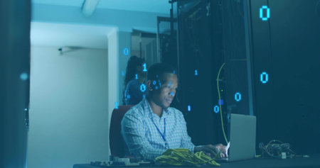 Typing man in checkered shirt, colleague inspecting servers in server room with laptop and cables....