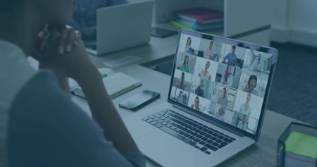 Mature Asian woman in grey top watching conference on laptop at desk, with copy space. Professional, teamwork, collaboration, modern, corporate, digital, communicationの写真素材